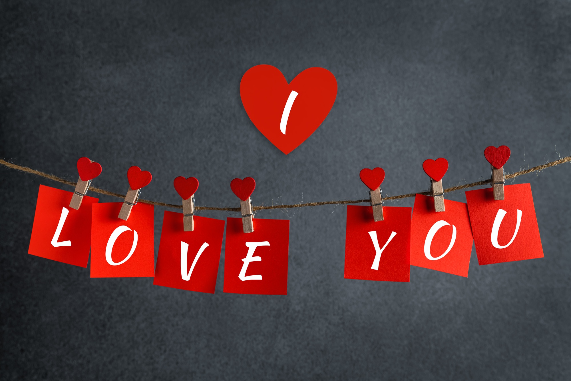 I love you on red square pieces of paper on grey background. clothespins in the form of hearts